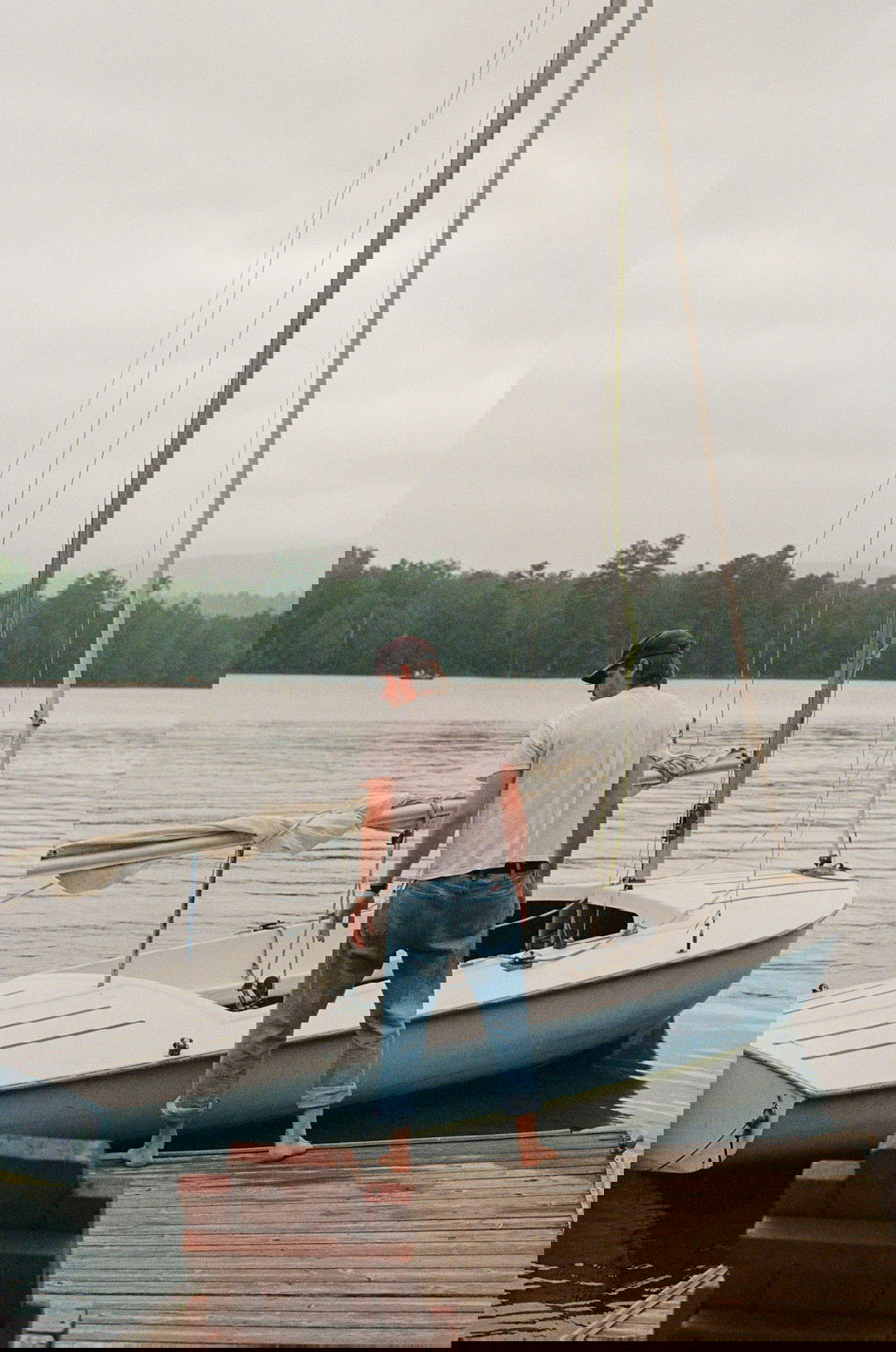 Man standing next to his sailboat at the dock.